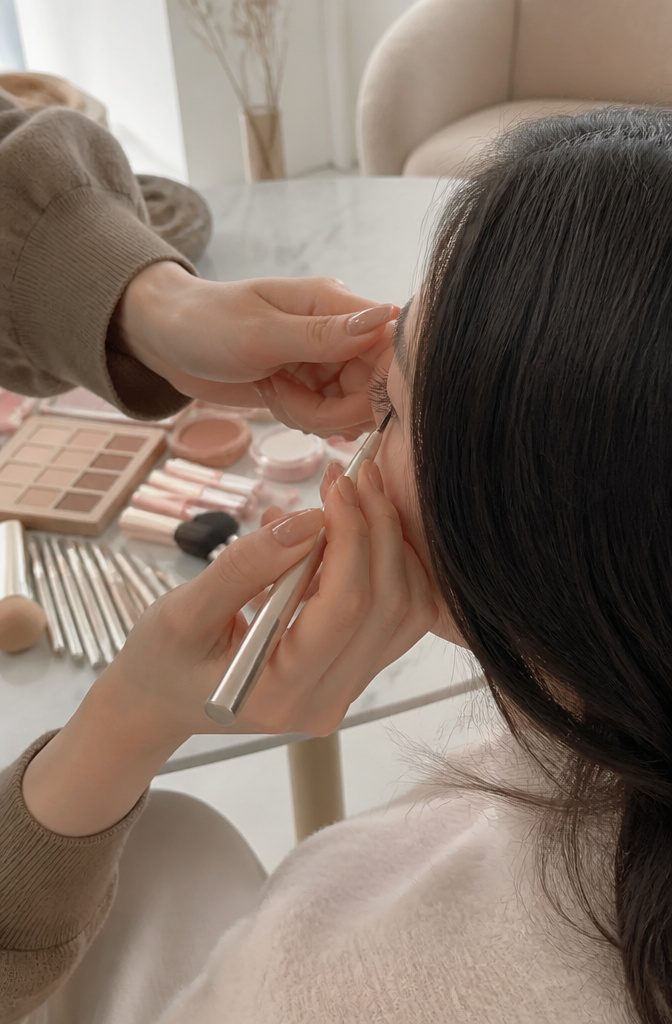 A close-up of a makeup artist applying glitter eyeliner to a model's lower lashes.